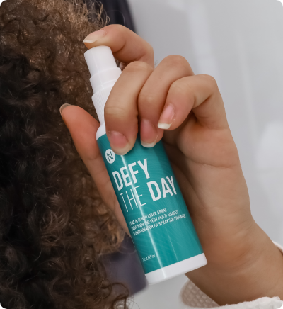 Hand holding Defy The Day Leave-In Conditioner up to hair